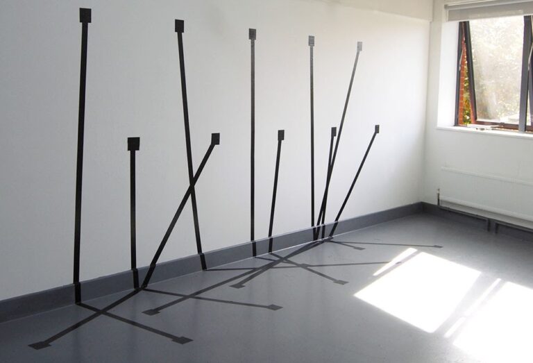 A minimalist art installation in a white-walled room features black tape arranged on the wall and floor to create an optical illusion of intersecting lines and rectangles, resembling an abstract artwork. Sunlight streams through a window, illuminating part of the display, casting intriguing shadows.